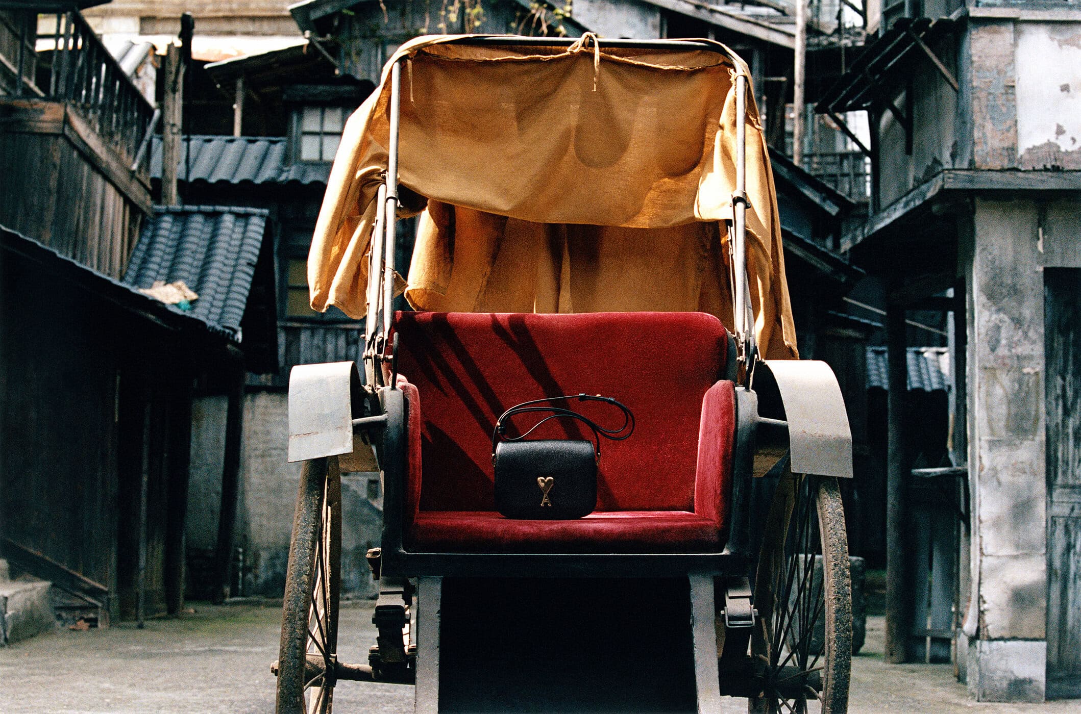 Black leather handbag resting on a red upholstered seat of a traditional rickshaw in an alleyway