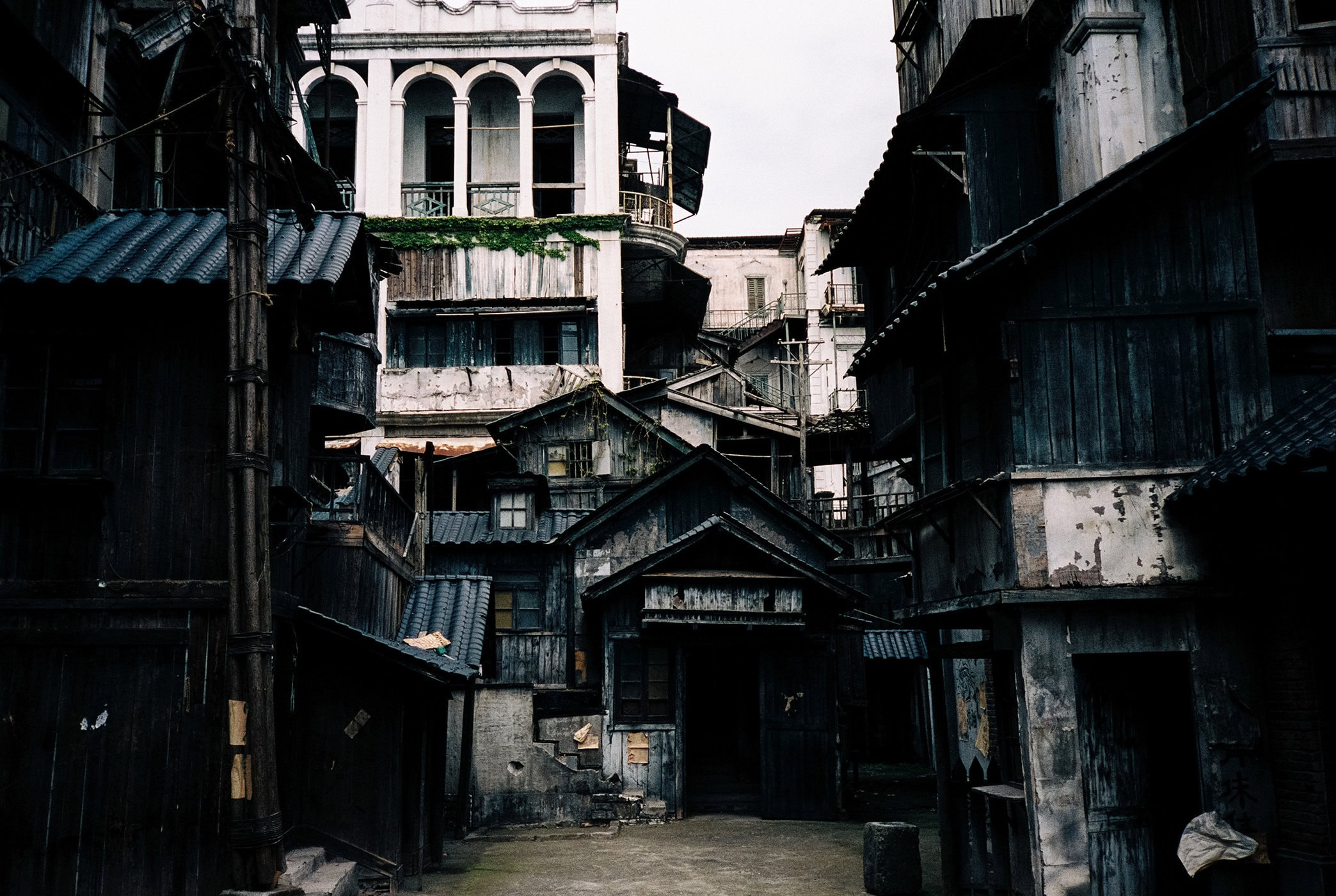 A narrow alleyway surrounded by dark wooden buildings and weathered architectural structures under an overcast sky.