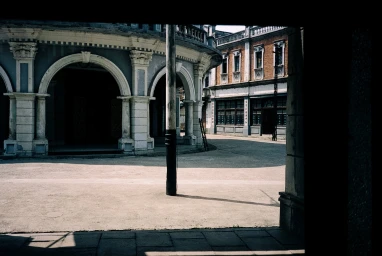 An outdoor square view framed by architectural archways and a central pole under natural daylight.