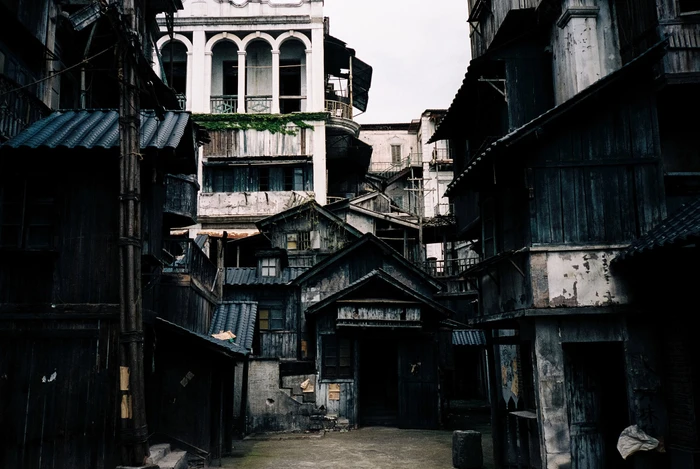 A narrow alleyway surrounded by dark wooden buildings and weathered architectural structures under an overcast sky.