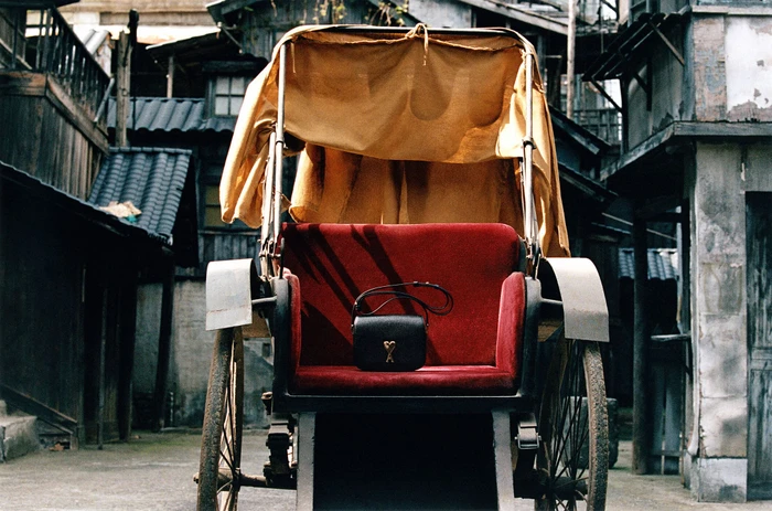 Black leather handbag resting on a red upholstered seat of a traditional rickshaw in an alleyway