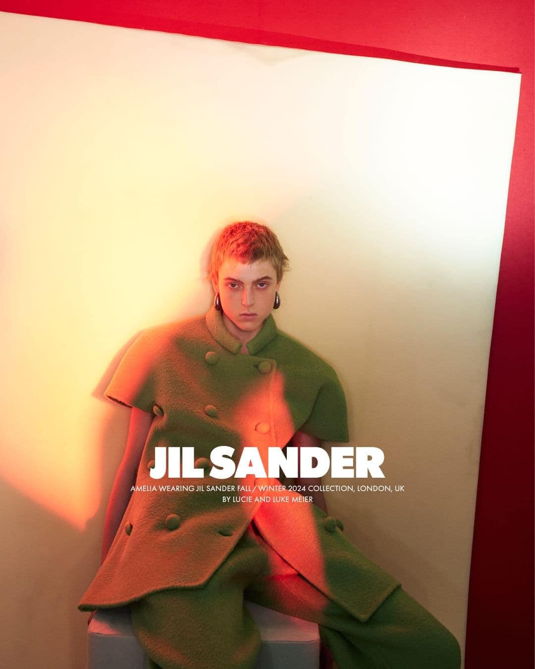 Model with short hair wearing a green textured double-breasted top against a white and red backdrop