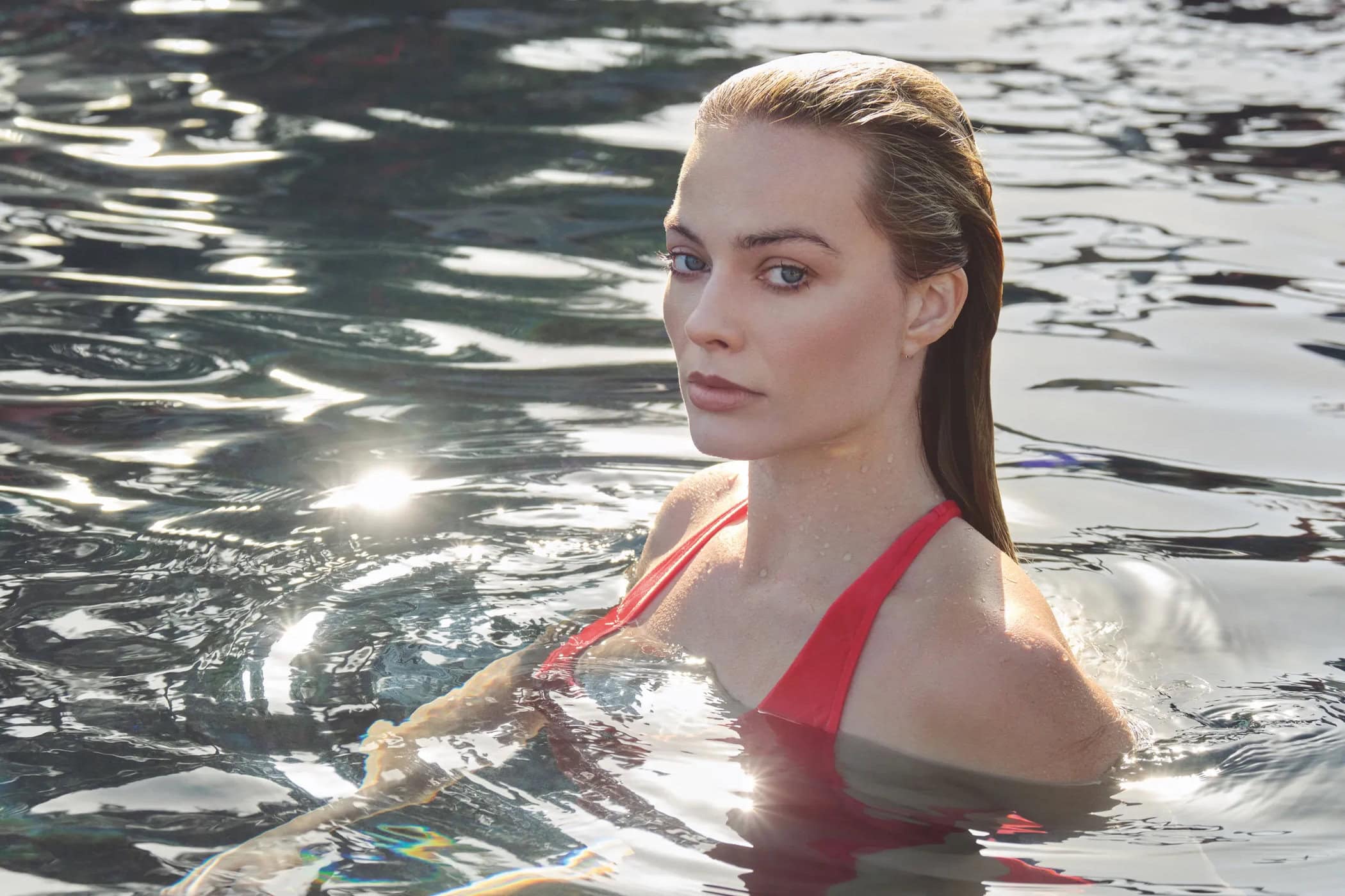Margot Robbie with wet slicked-back hair wearing a red swimsuit in a dark outdoor pool for Chanel ad campaign
