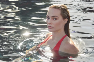 Margot Robbie with wet slicked-back hair wearing a red swimsuit in a dark outdoor pool for Chanel ad campaign