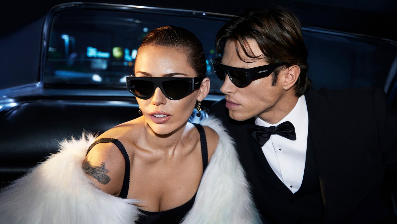 Miley Cyrus and a man wearing black sunglasses inside a dark vehicle for a Dolce and Gabbana campaign