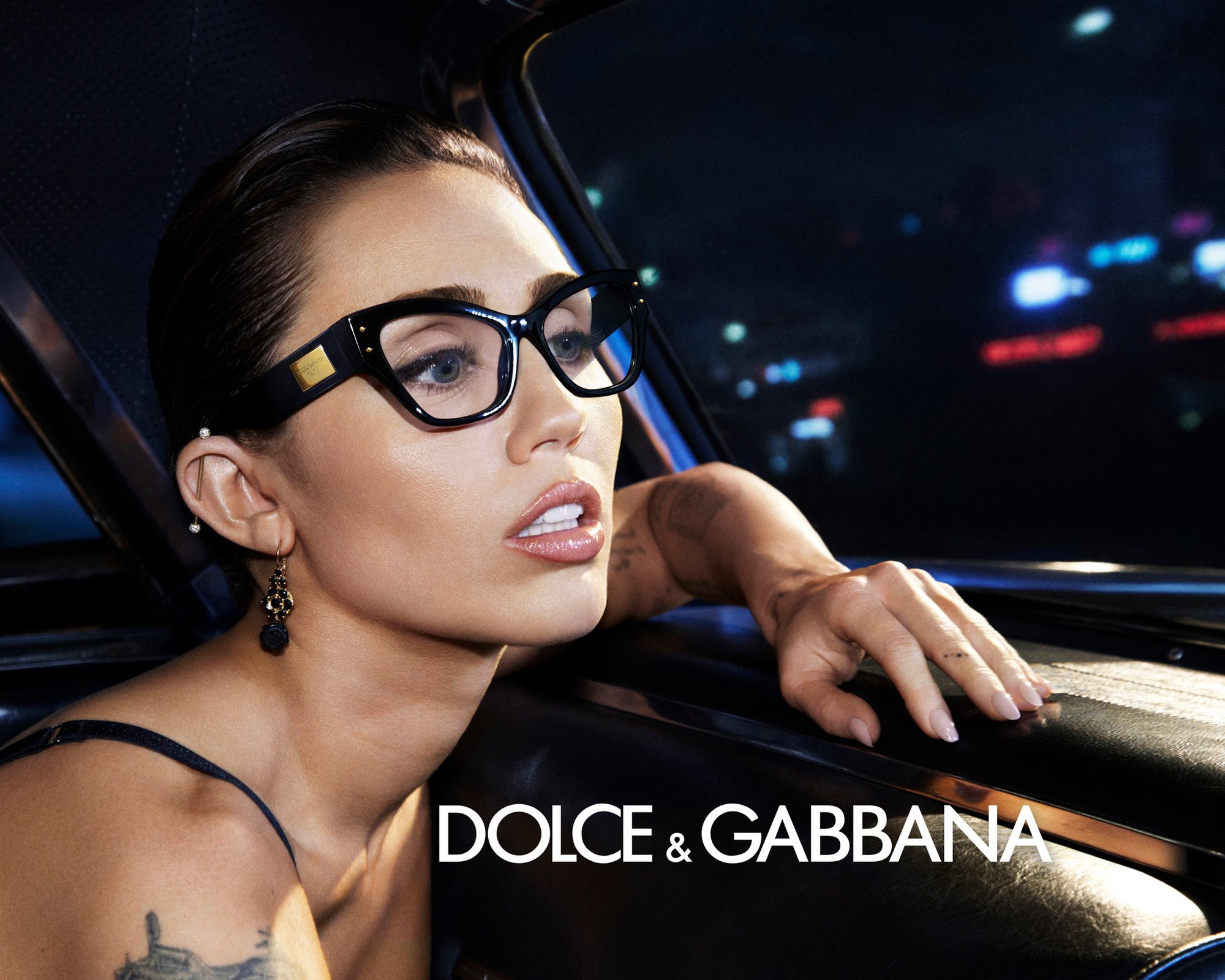 Miley Cyrus wearing black cat-eye glasses inside a car at night for Dolce and Gabbana campaign