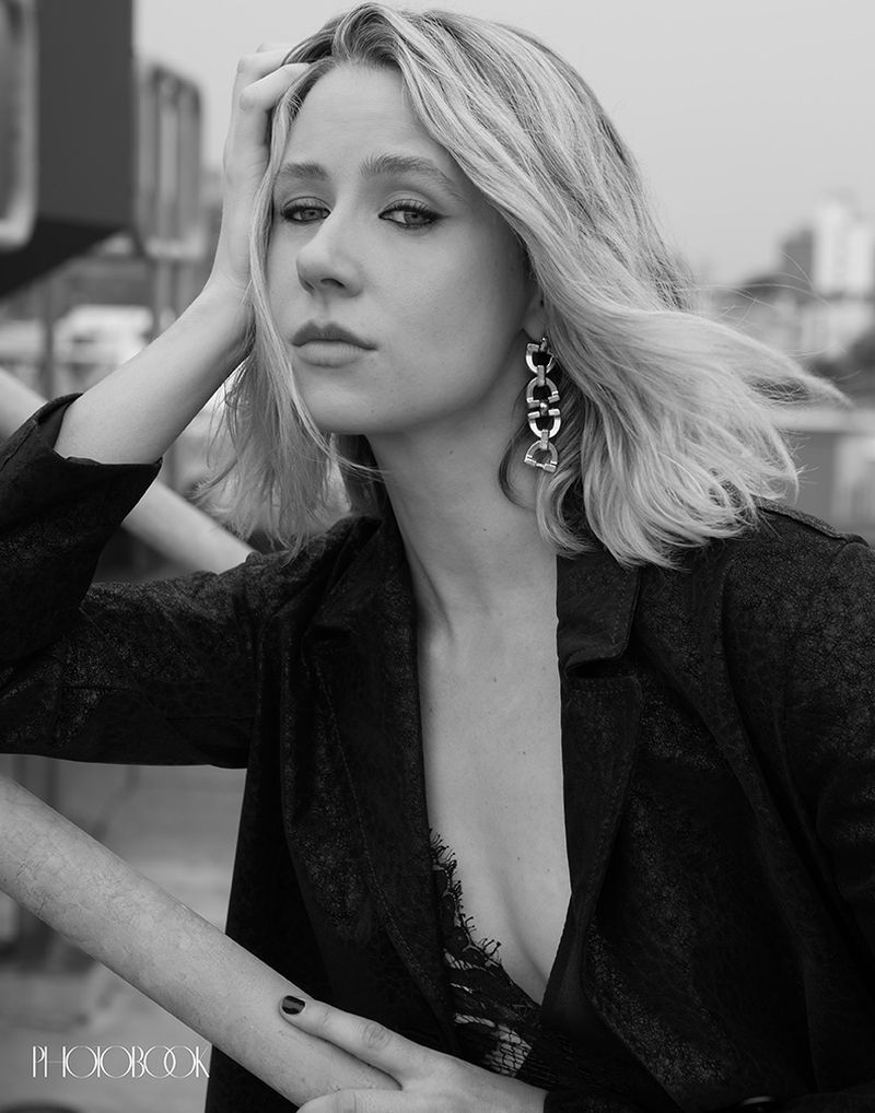 Portrait of a blonde woman in a black blazer and lace top outdoors, with modern architecture in the background, shot in black and white.
