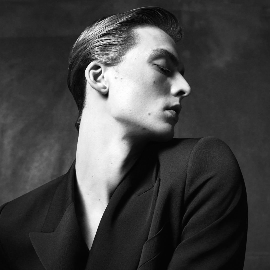 Close-up portrait of model Leon Dame wearing a dark jacket against a textured dark background for Dolce & Gabbana