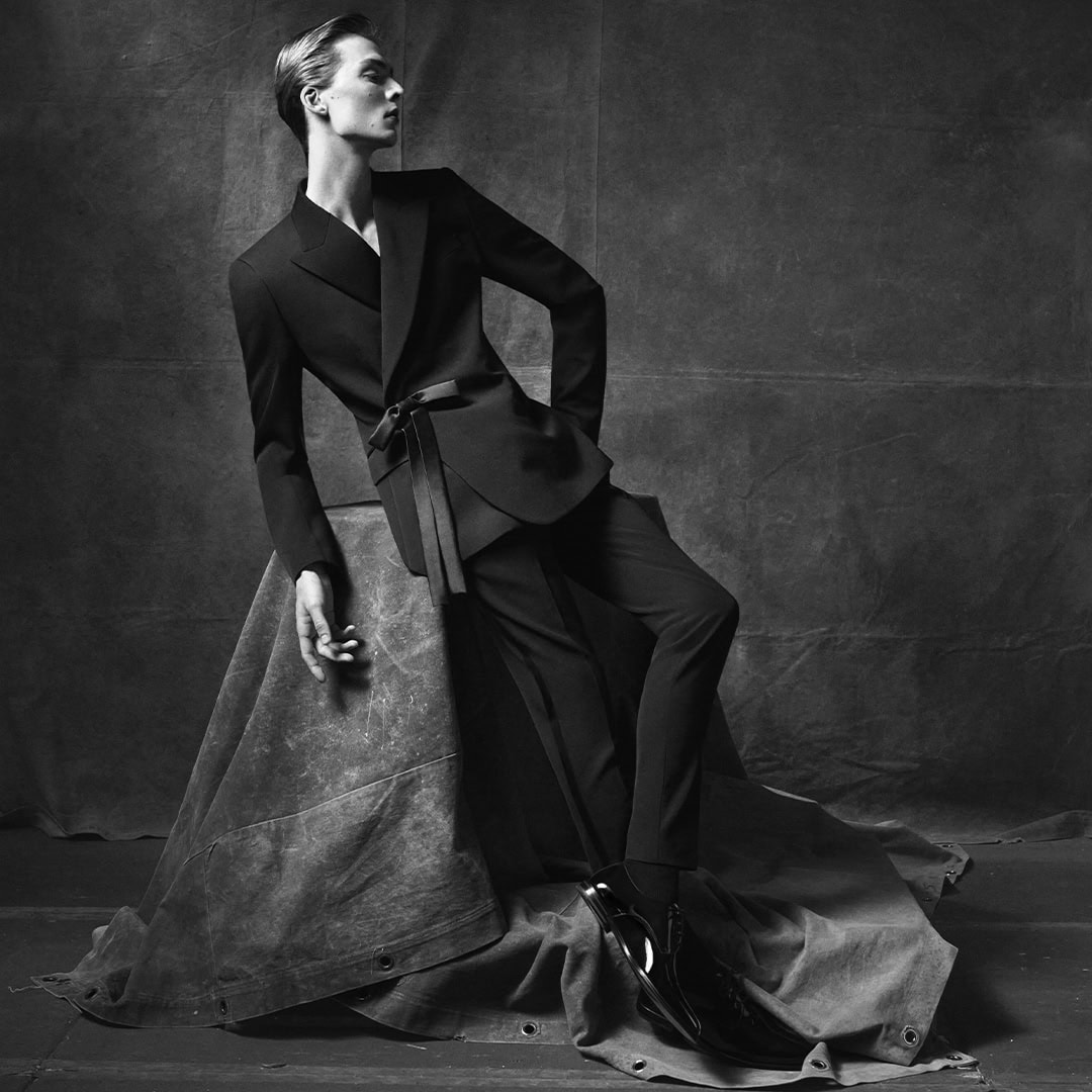 Model Leon Dame in a black suit leaning against a draped prop for Dolce and Gabbana campaign