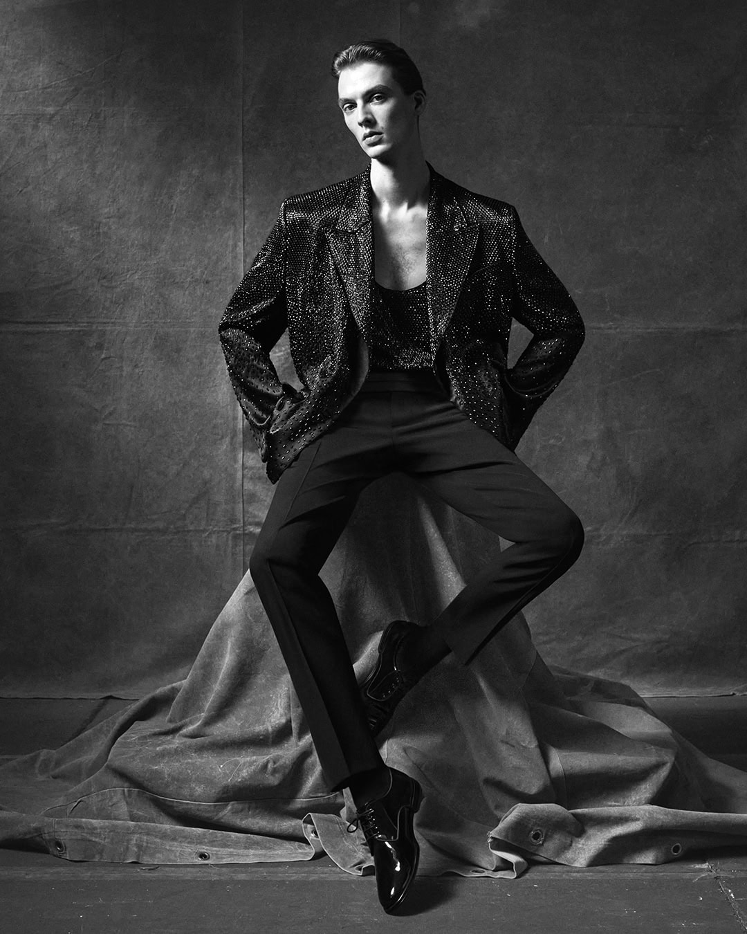 Model Leon Dame seated on draped fabric wearing a dark textured blazer for Dolce and Gabbana campaign