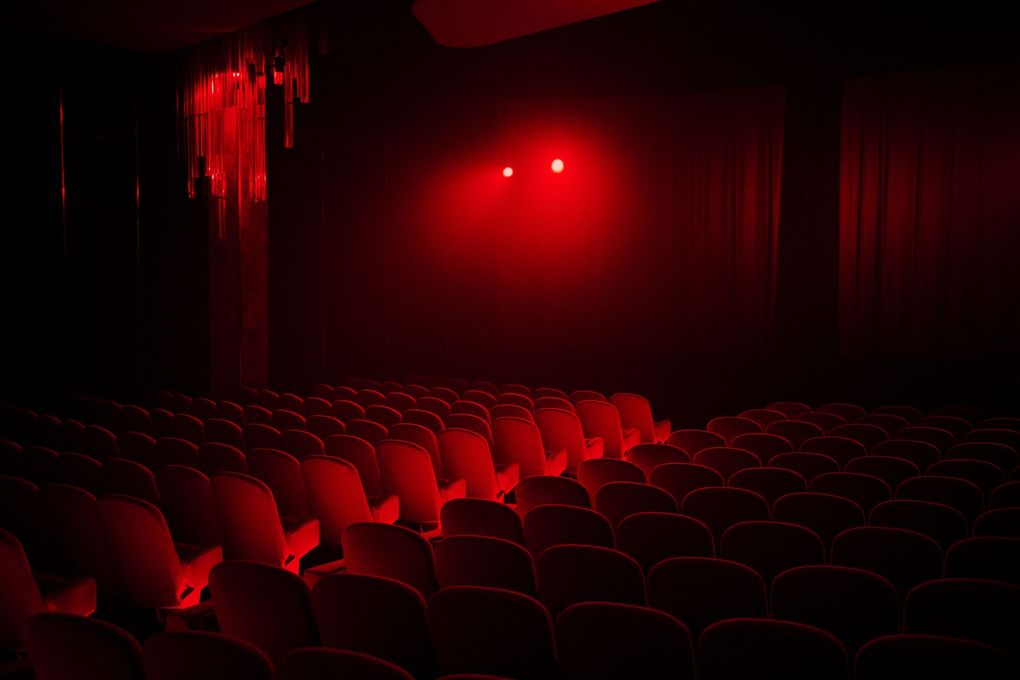 Empty cinema auditorium with rows of red velvet seats illuminated by dramatic red spotlights in Maison Margiela Nighthawk campaign