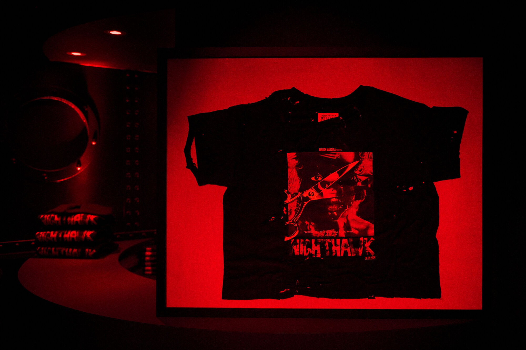 Distressed black t-shirt with graphic print displayed in an illuminated red frame for Maison Margiela campaign.
