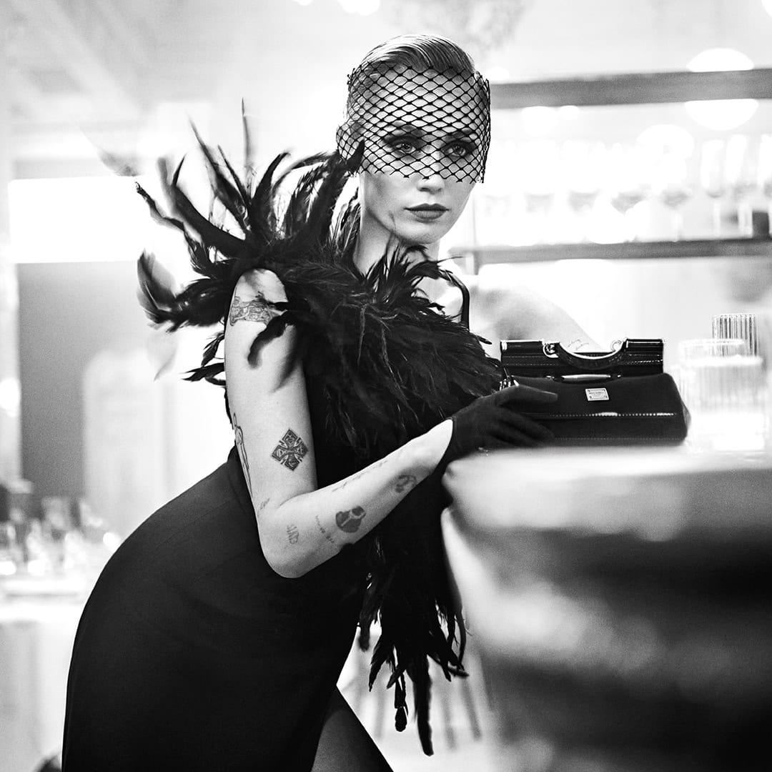 Miley Cyrus wearing a black feather dress and net veil leaning against a bar for Dolce & Gabbana
