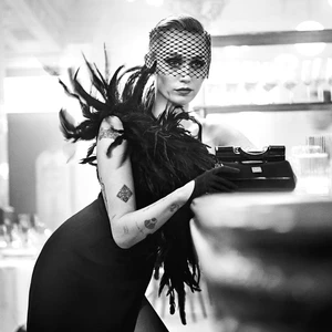 Miley Cyrus wearing a black feather dress and net veil leaning against a bar for Dolce & Gabbana