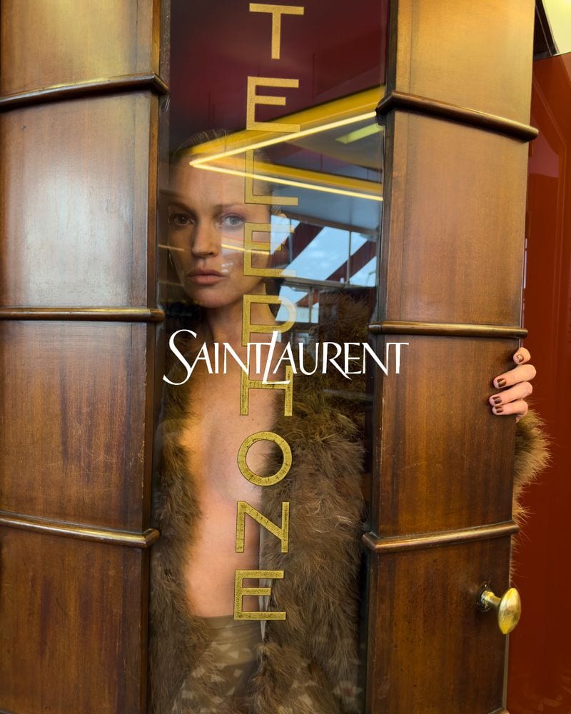 Kate Moss framed inside a wooden telephone booth wearing a furry coat for Saint Laurent Winter 2024 campaign