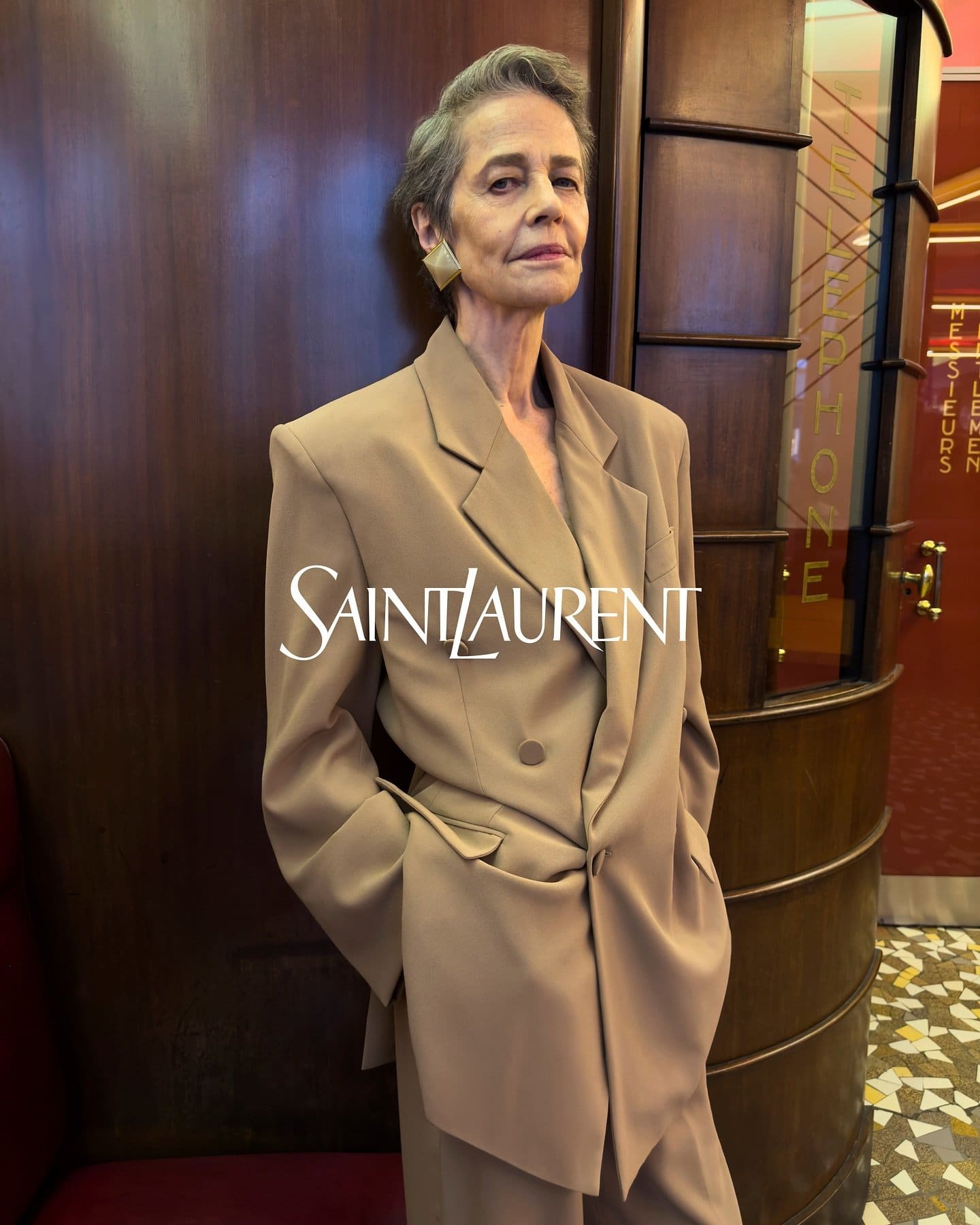Charlotte Rampling wearing an oversized camel blazer in a wood-paneled interior for Saint Laurent Winter 2024 campaign
