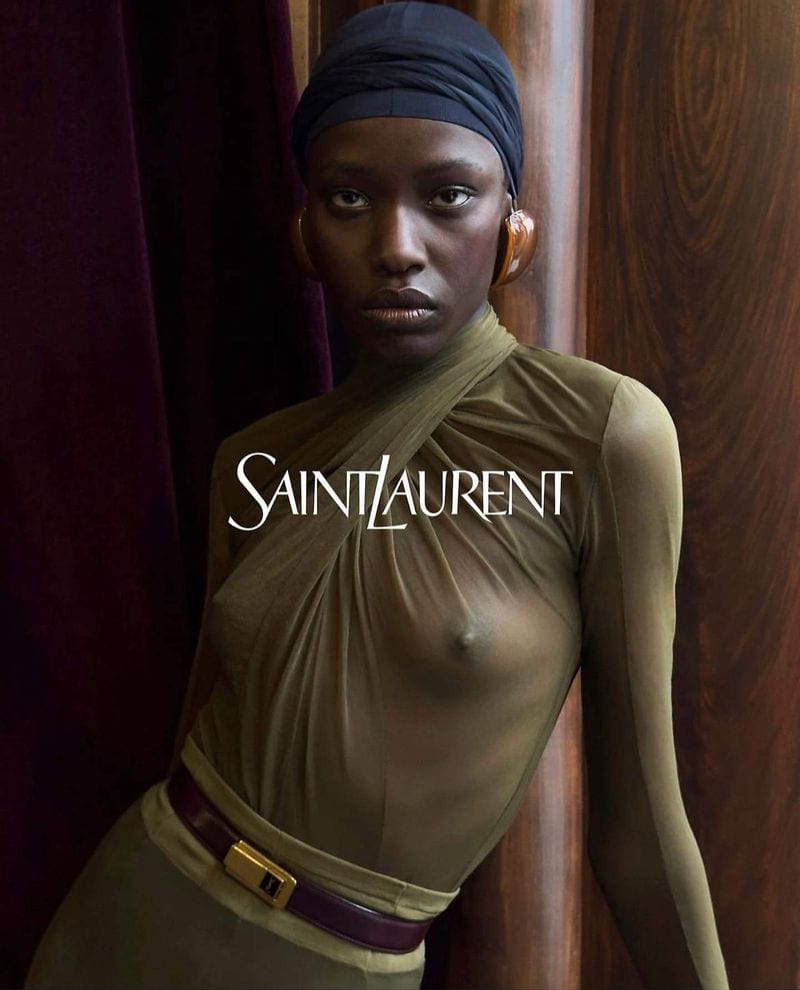 Black model wearing an olive green sheer top, dark headwrap, and burgundy belt for Saint Laurent winter campaign