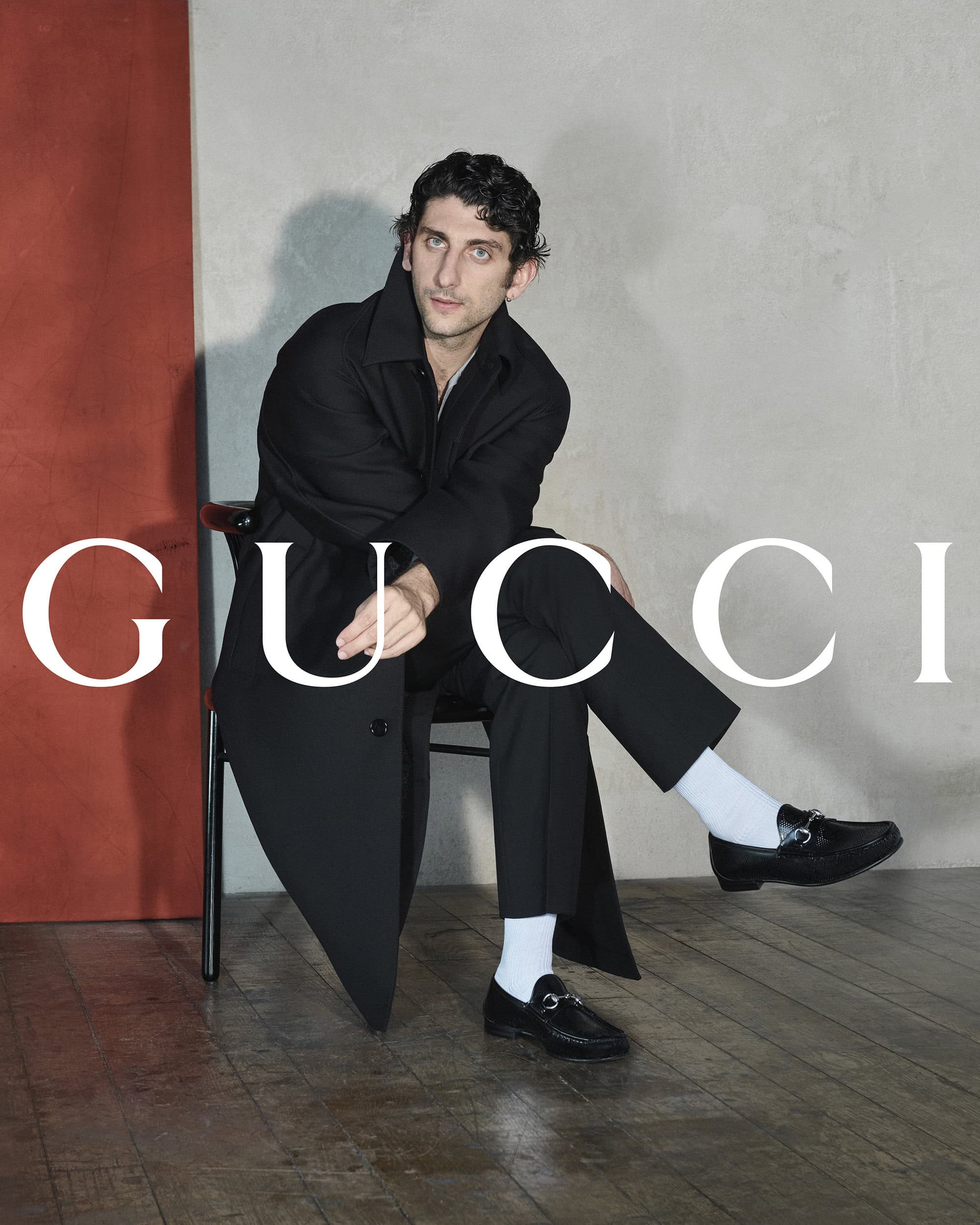 Pietro Castellitto seated wearing a black coat and loafers for Gucci The Loafer Since 1953 campaign