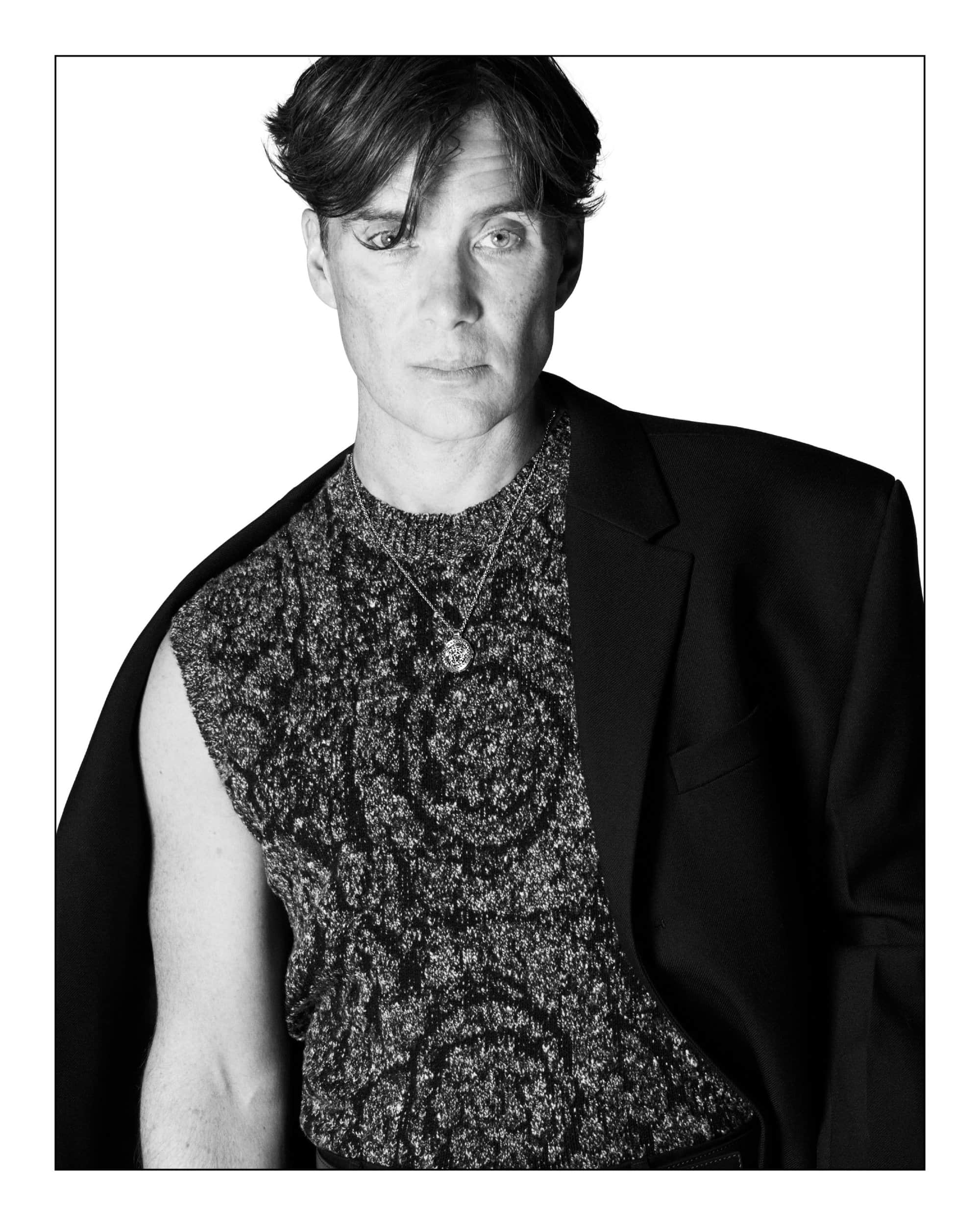 Monochrome portrait of Cillian Murphy in a patterned sleeveless knit top and dark blazer against a white backdrop.