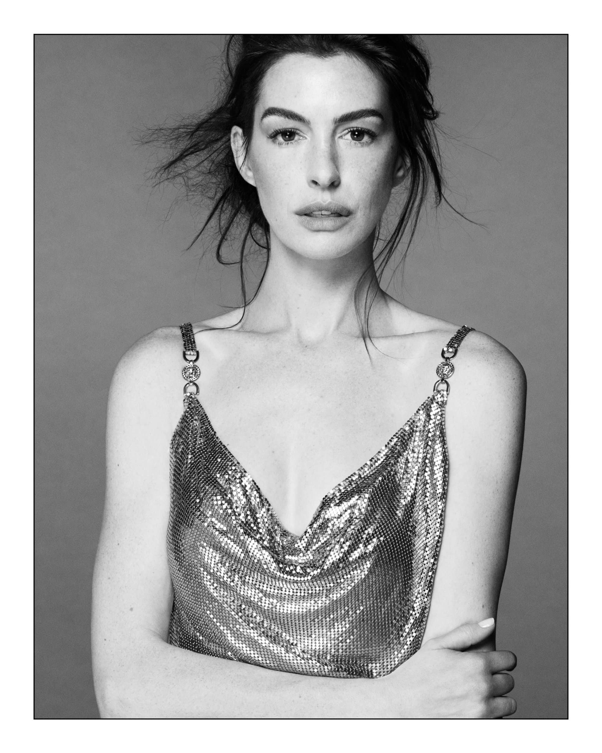 Monochrome portrait of Anne Hathaway in a chainmail strap top against a seamless grey backdrop for Versace.