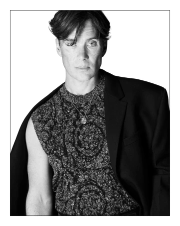 Monochrome portrait of Cillian Murphy in a patterned sleeveless knit top and dark blazer against a white backdrop.