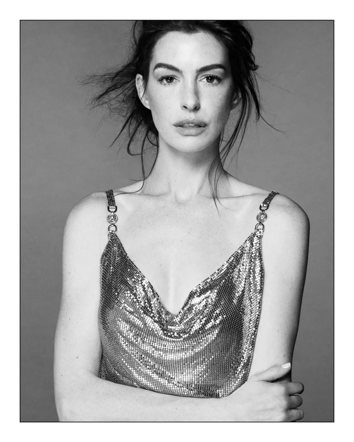 Monochrome portrait of Anne Hathaway in a chainmail strap top against a seamless grey backdrop for Versace.