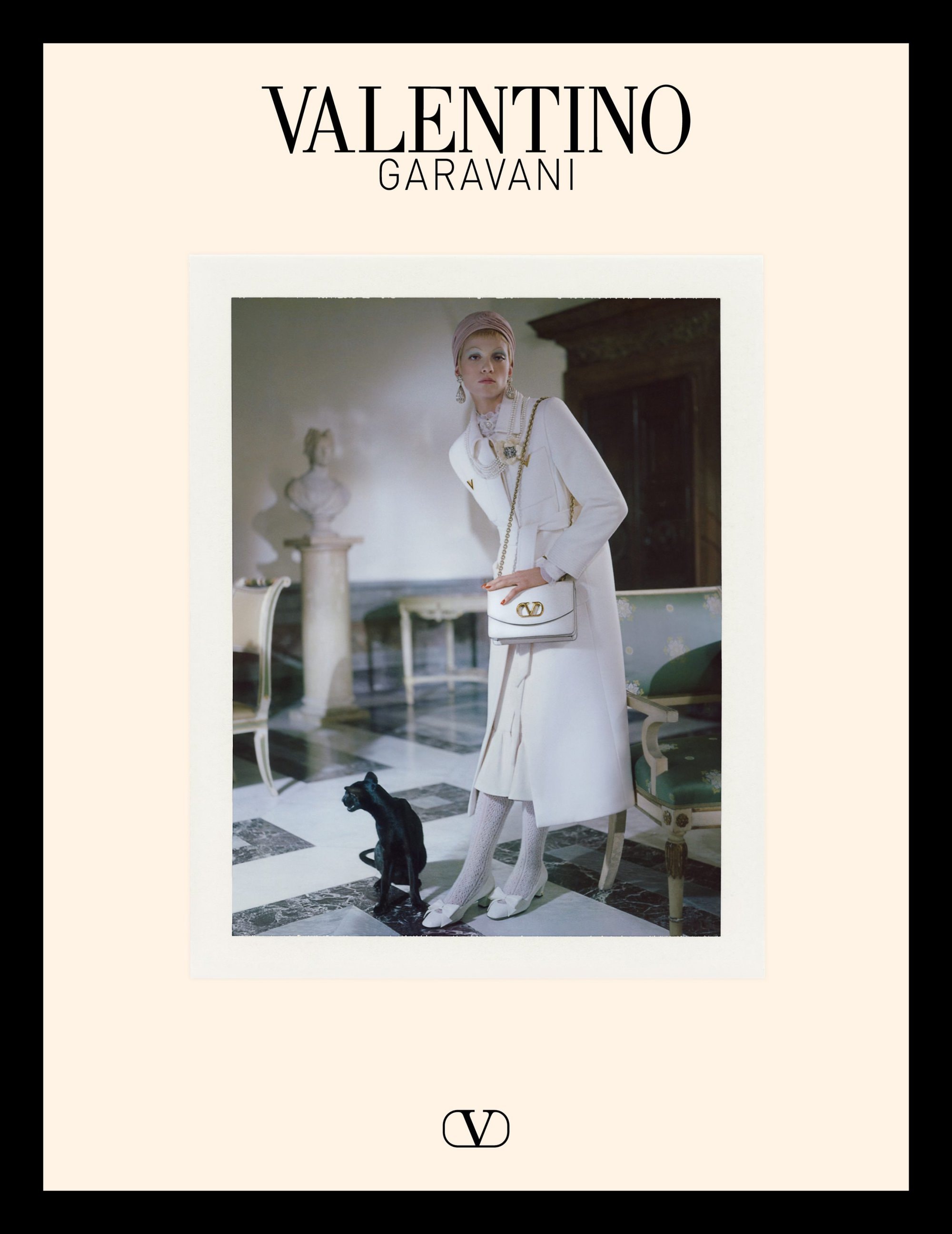 Model in a white coat and matching handbag posing indoors in an elegant room for Valentino Resort 2025 campaign.