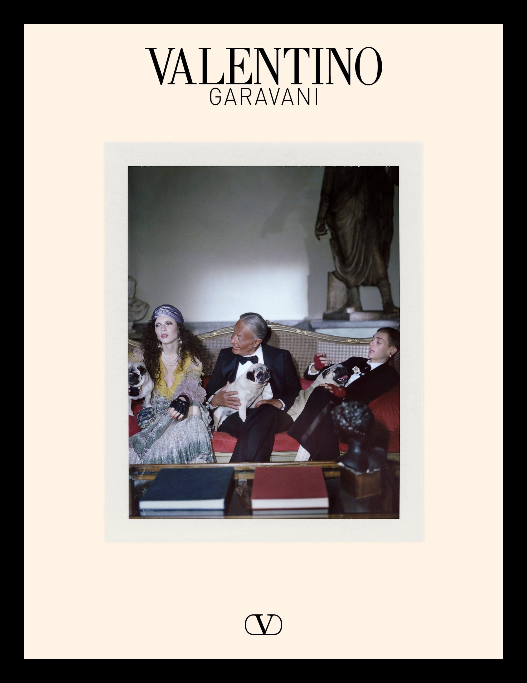 Three models holding pugs on a red sofa beneath a classical statue for Valentino