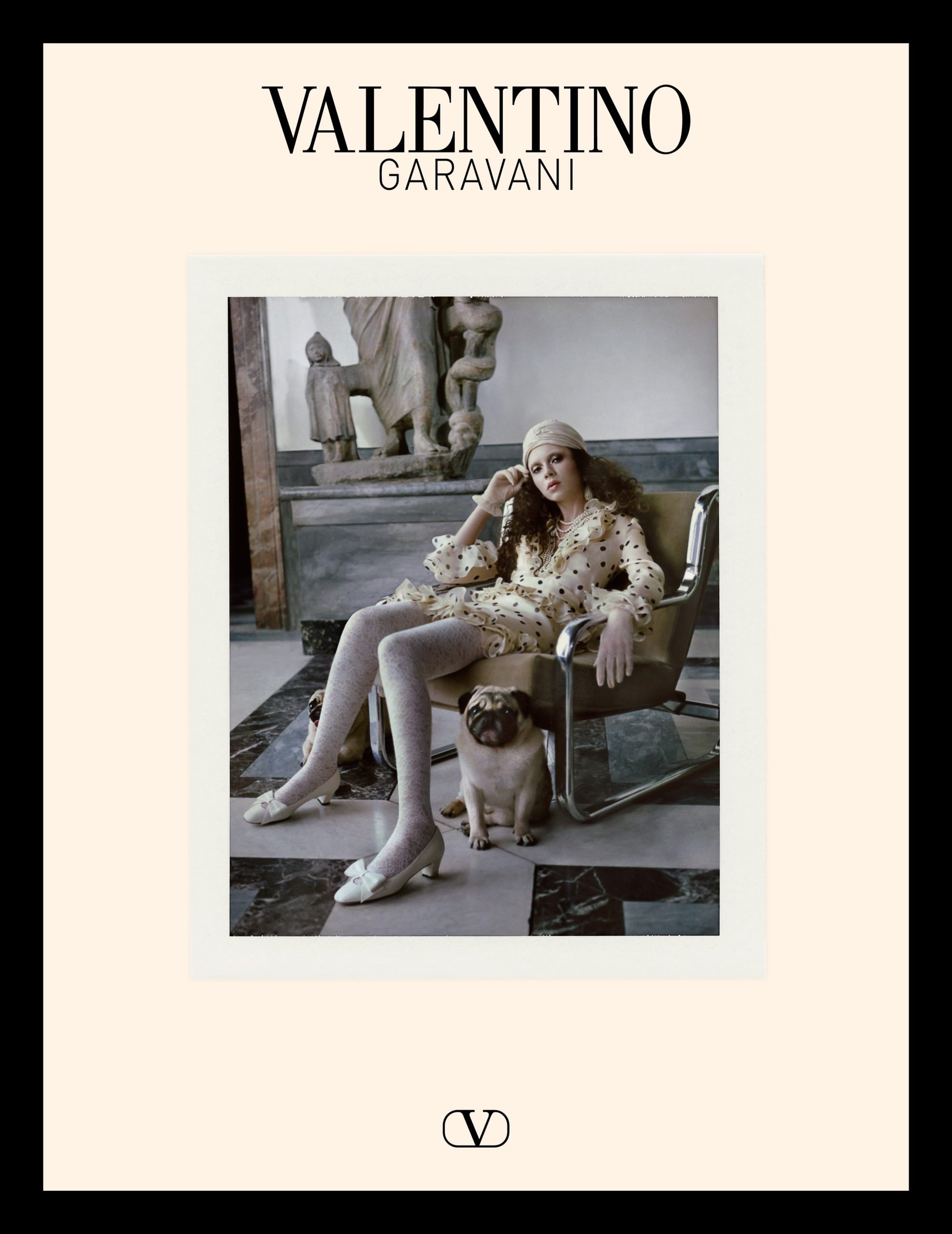 Model seated in an armchair wearing a patterned dress with pugs at her feet for Valentino
