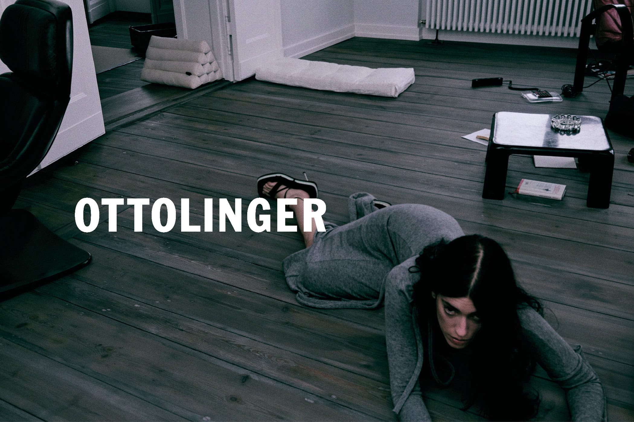 Woman in grey long-sleeve dress lying on a dark wooden floor inside a room