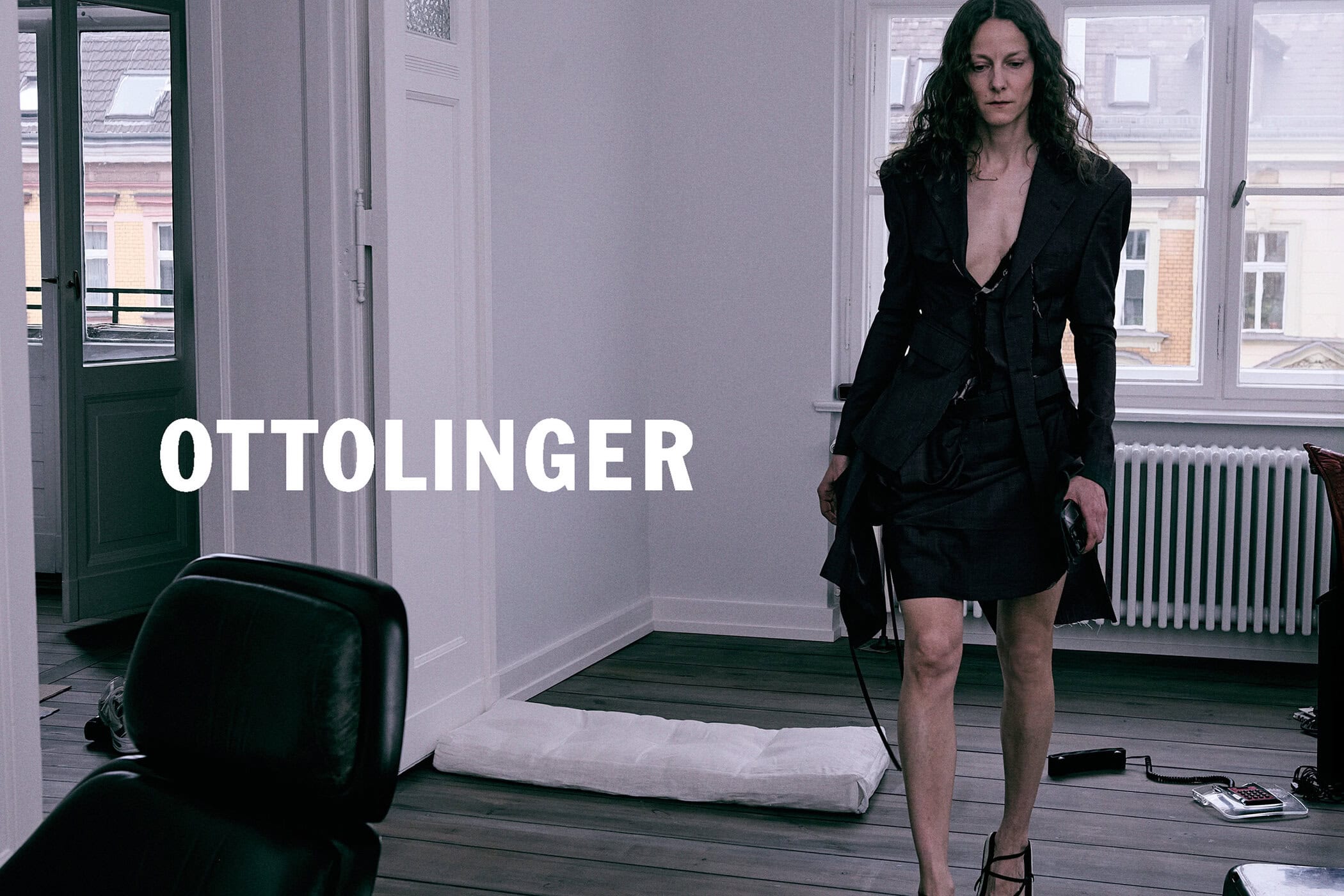 Woman in dark blazer and skirt walking across a room in an apartment interior for Ottolinger Fall 2024 campaign