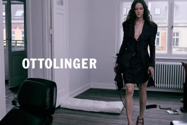 Woman in dark blazer and skirt walking across a room in an apartment interior for Ottolinger Fall 2024 campaign