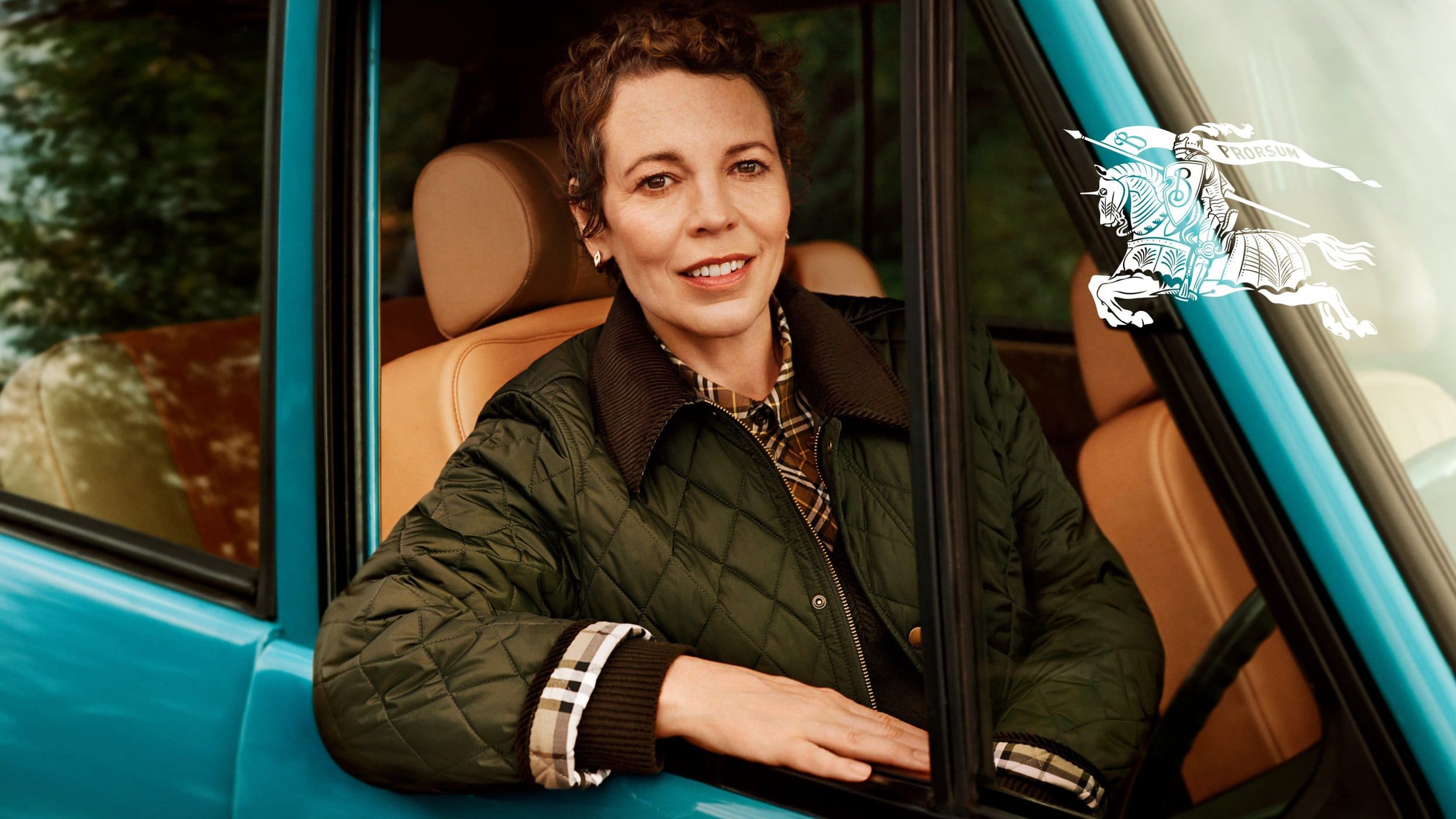 Olivia Colman wearing a green quilted jacket sitting inside a bright blue car for Burberry campaign