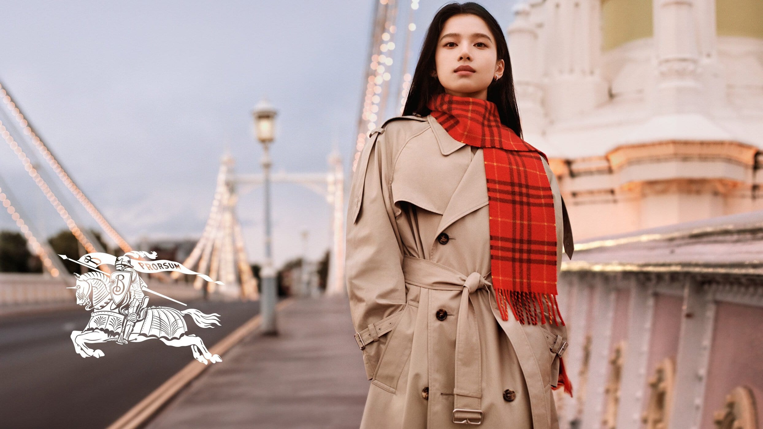 Zhang Jingyi wearing a beige trench coat and red plaid scarf on a bridge for Burberry.