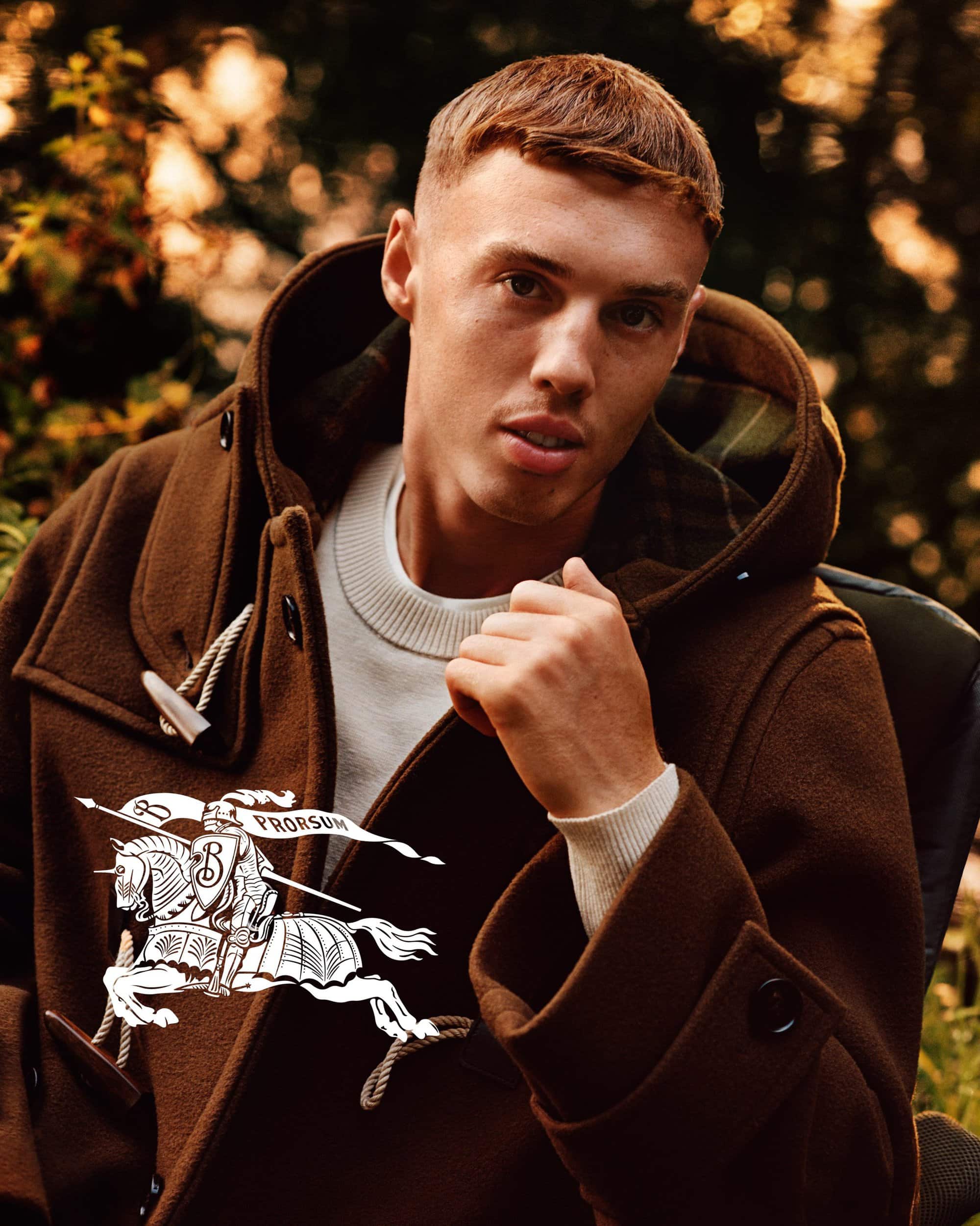 Cole Palmer wearing a brown duffle coat over a white sweater in an outdoor Burberry advertising campaign photograph.