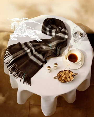 Burberry plaid scarf draped on a white clothed café table with a cup of coffee and sugar bowl