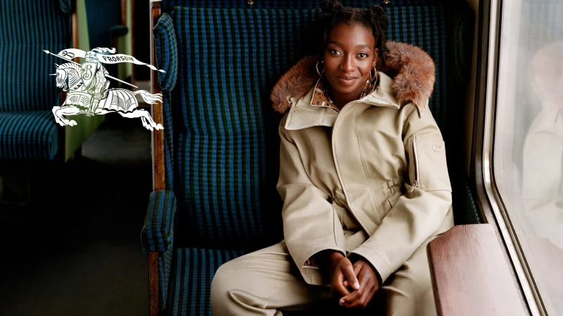 Little Simz seated in a train carriage wearing a tan parka with fur hood for Burberry