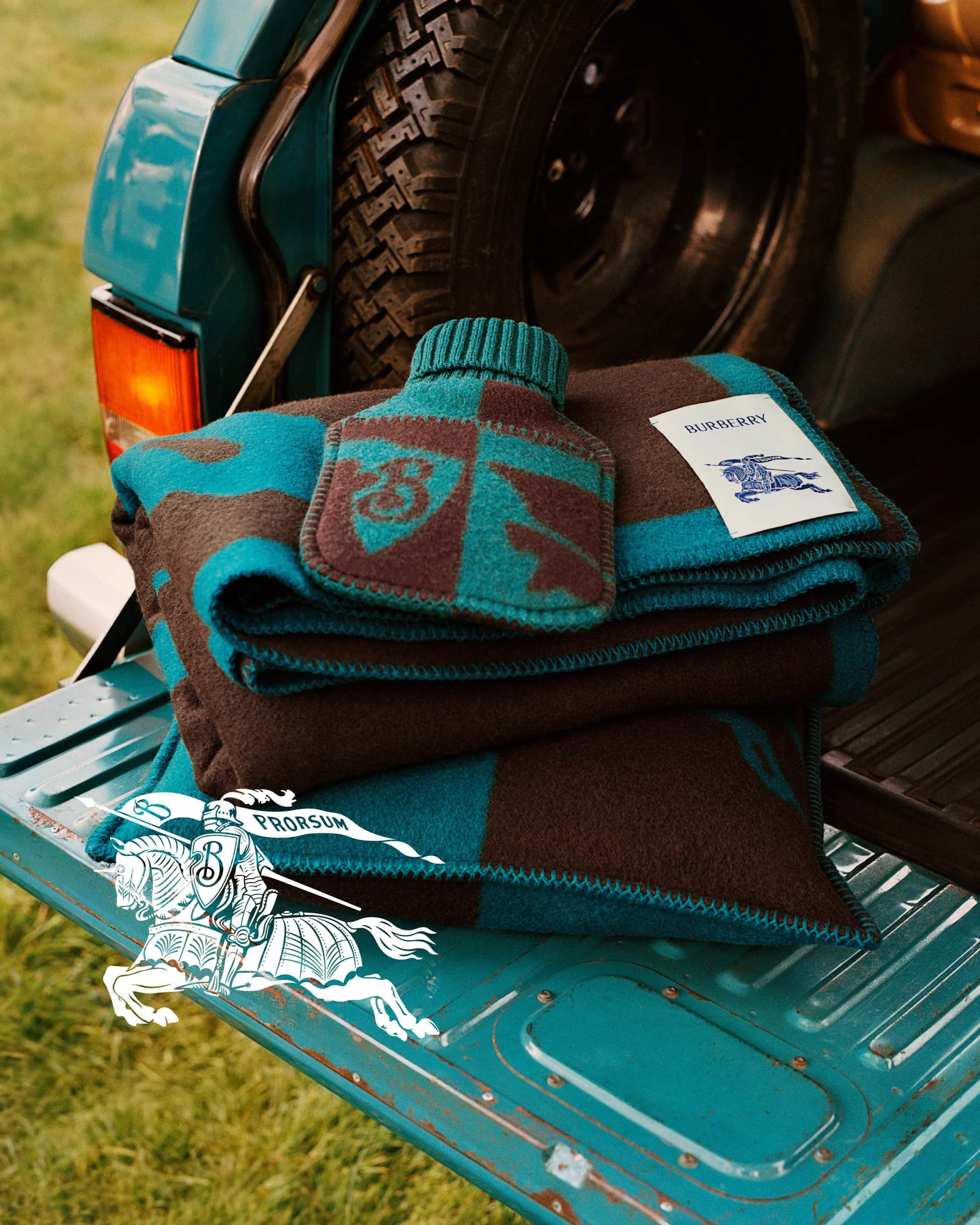 Folded blue and brown patterned blanket with matching hot water bottle in the open tailgate of a vehicle