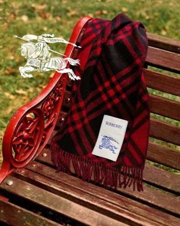 Red and black plaid scarf draped over a wooden park bench with a visible Burberry logo tag