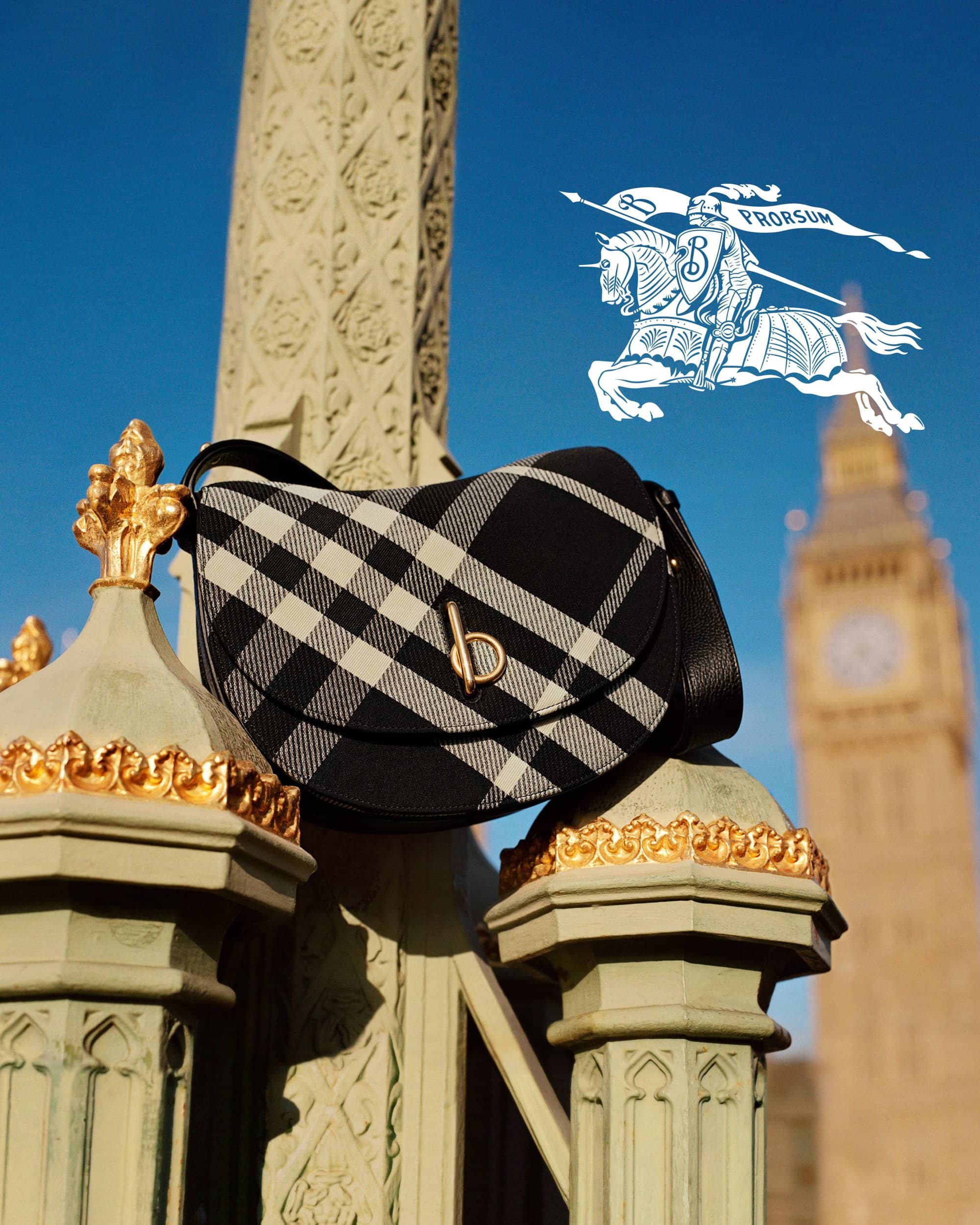 Burberry black and white plaid handbag resting on ornate architectural stonework against a clear blue sky with Big Ben in the background.