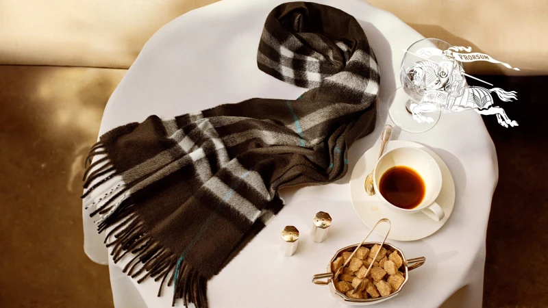 Burberry plaid scarf resting on a small white table with a cup of coffee and sugar cubes