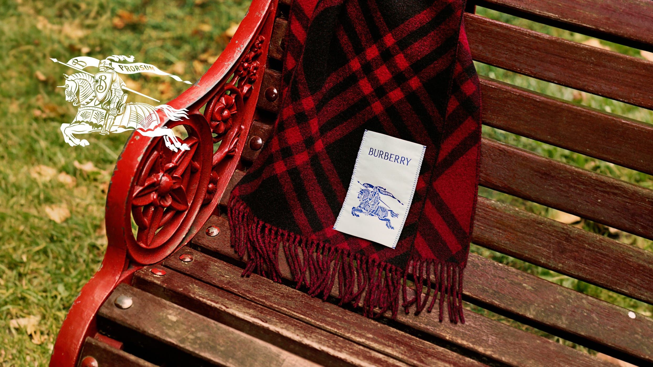 Red and black plaid Burberry scarf draped over a wooden park bench with a visible branded label