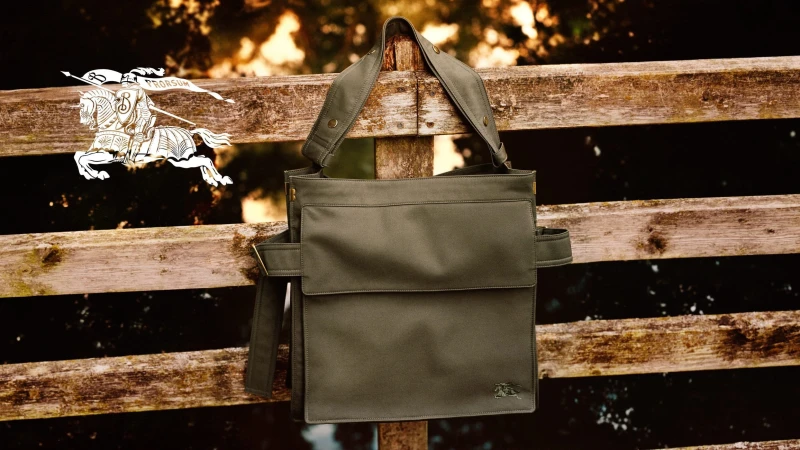 Olive green canvas shoulder bag hanging on a weathered wooden fence with a white equestrian logo graphic.