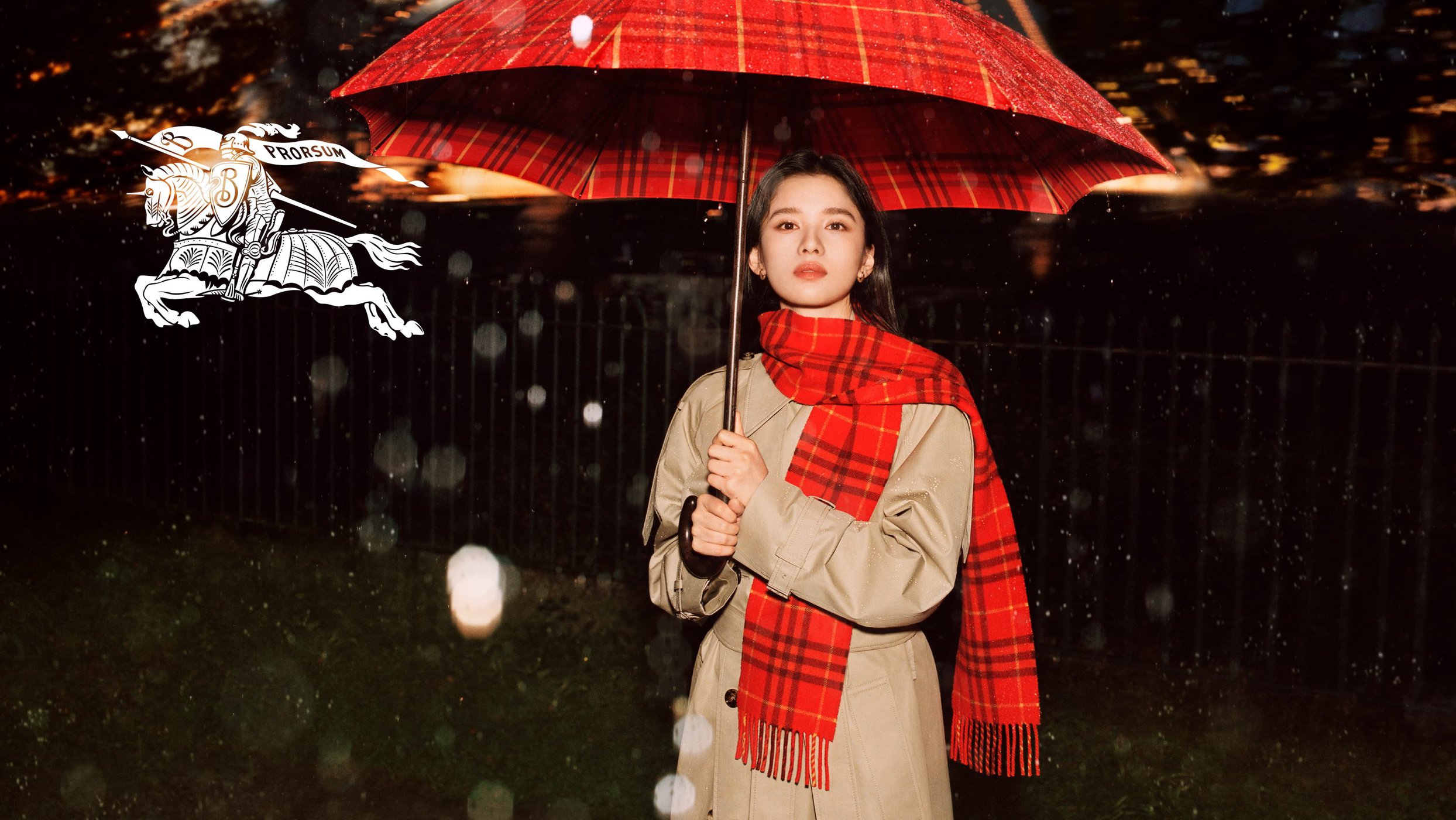 Zhang Jingyi holding a red plaid umbrella and wearing a trench coat and scarf under falling rain for Burberry