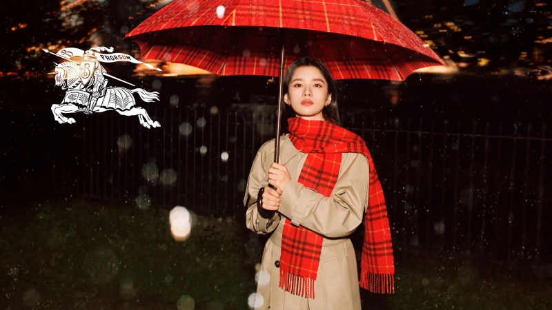 Zhang Jingyi holding a red plaid umbrella and wearing a trench coat and scarf under falling rain for Burberry