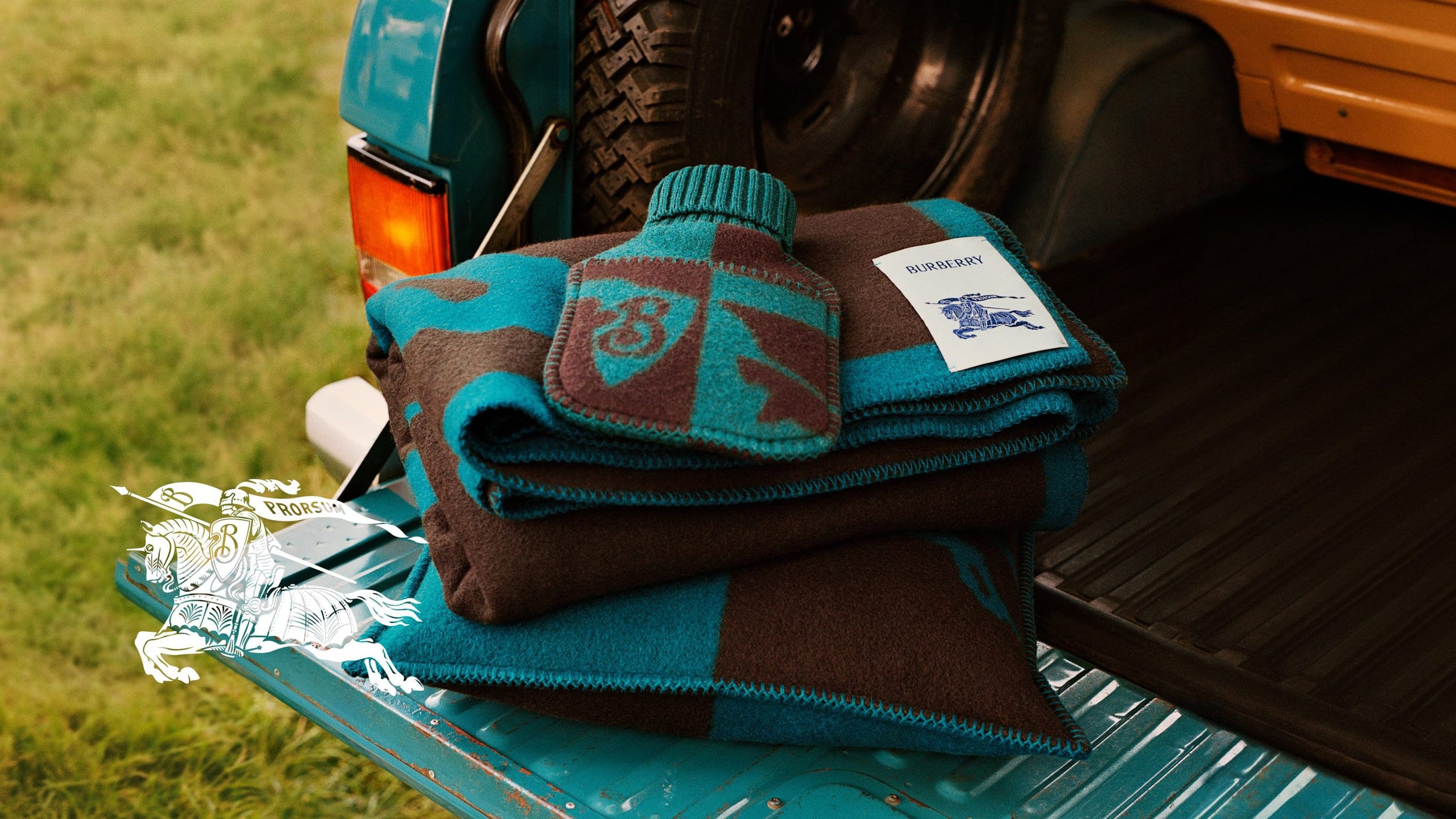 Folded blue and brown wool blanket with a matching hot water bottle resting on the open tailgate of a teal truck