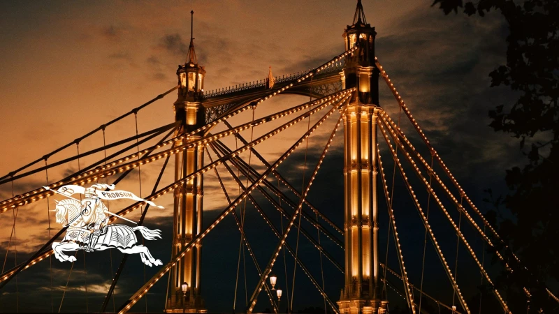 Illuminated suspension bridge towers at dusk with warm string lights outlining the cables and structural elements.