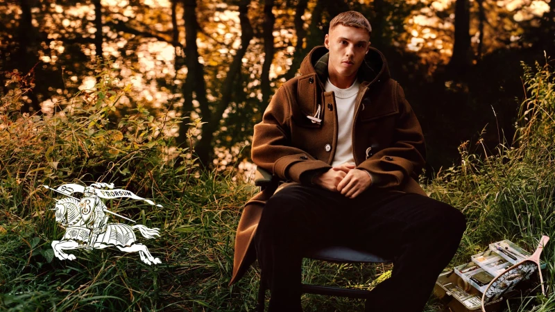 Cole Palmer seated outdoors in a brown duffle coat amidst autumn foliage for the Burberry 2024 campaign