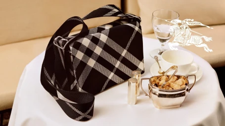 Black and white check handbag resting on a white tablecloth next to a silver sugar bowl and teacup.
