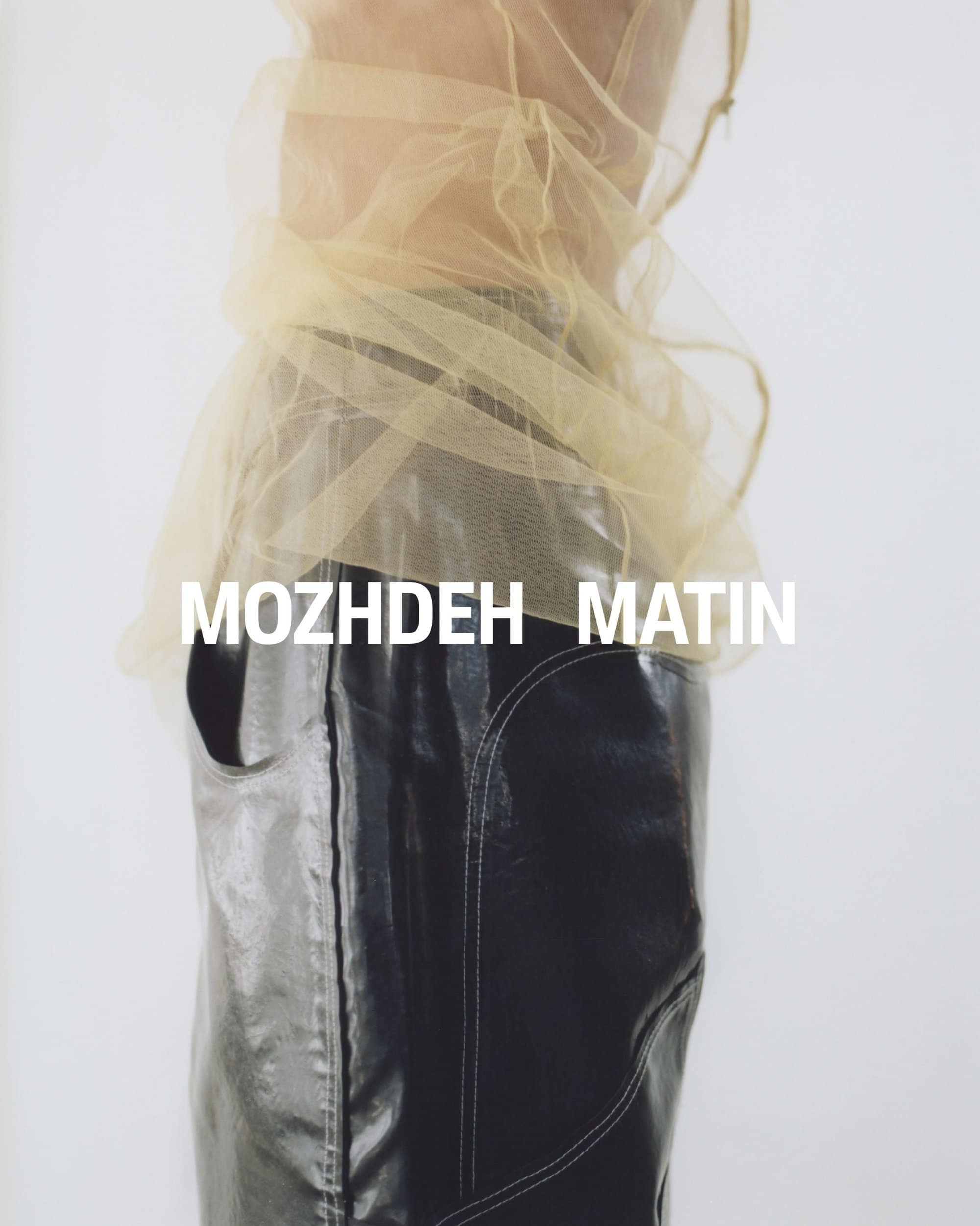 Model wearing sheer yellow top and black trousers against white background with brand text Mozhdeh Matin